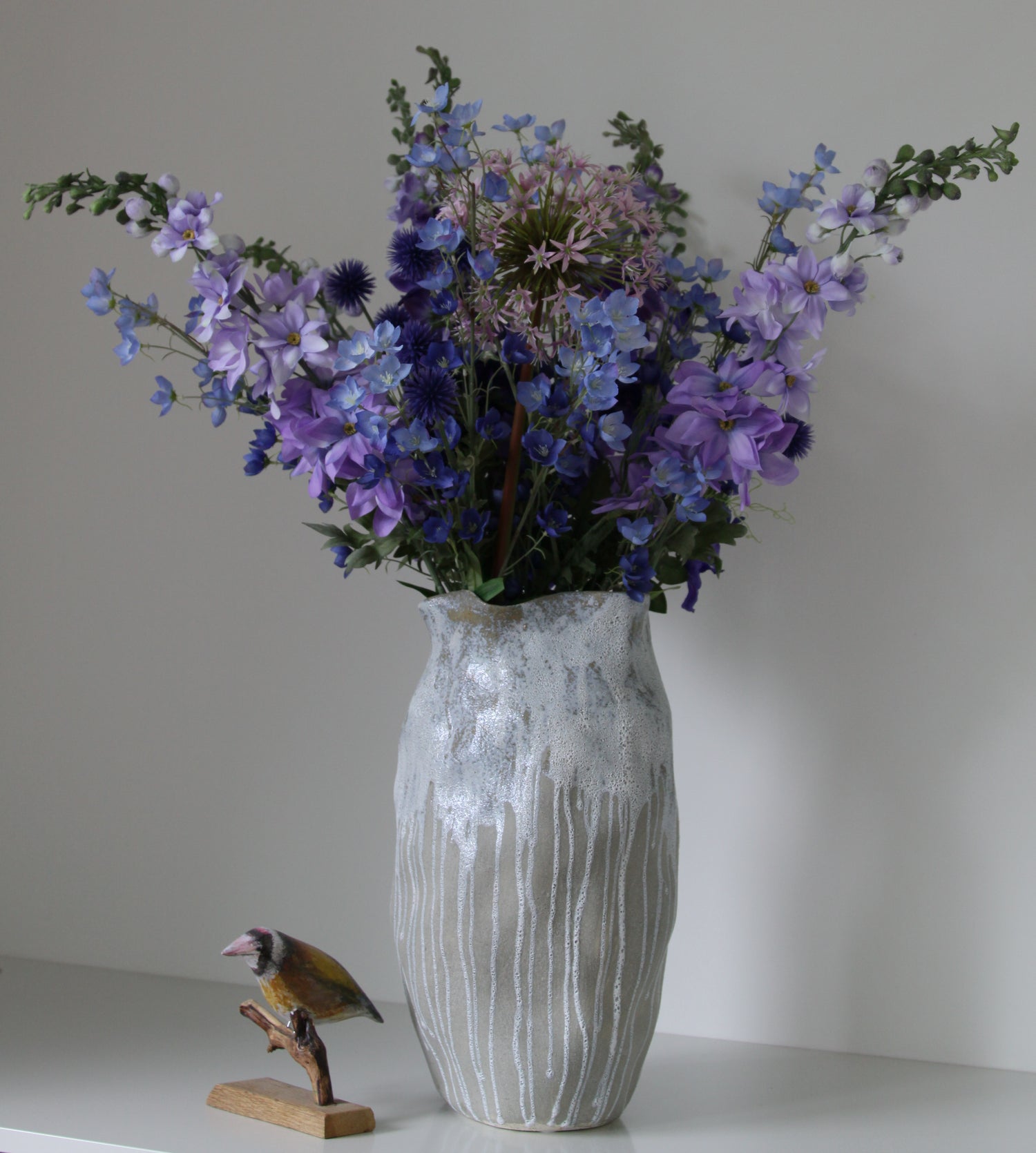 Vase mit Kunstblumen und einem Holzvogel auf einer Kommode